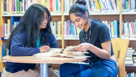 Two female students reading at a desk in the library. st helens sixth form