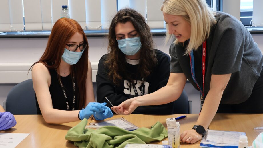 Female tutor and 2 female students working in the Criminology classroom with face masks on looking at evidence