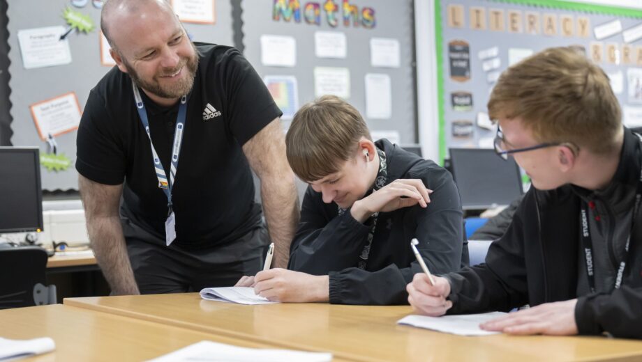 Male teacher stood smiling with two male students