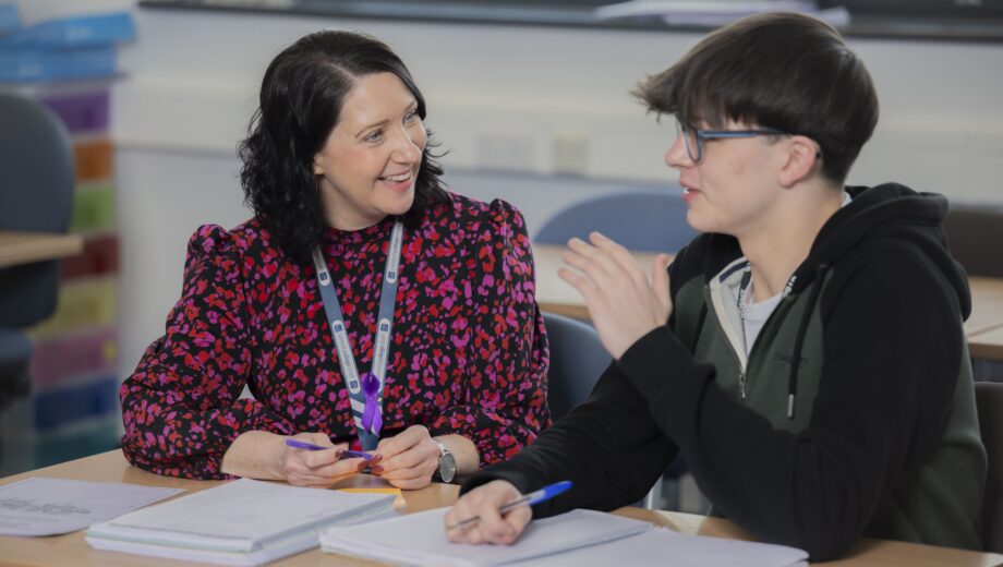 Female teacher and male student sat at a desk talking