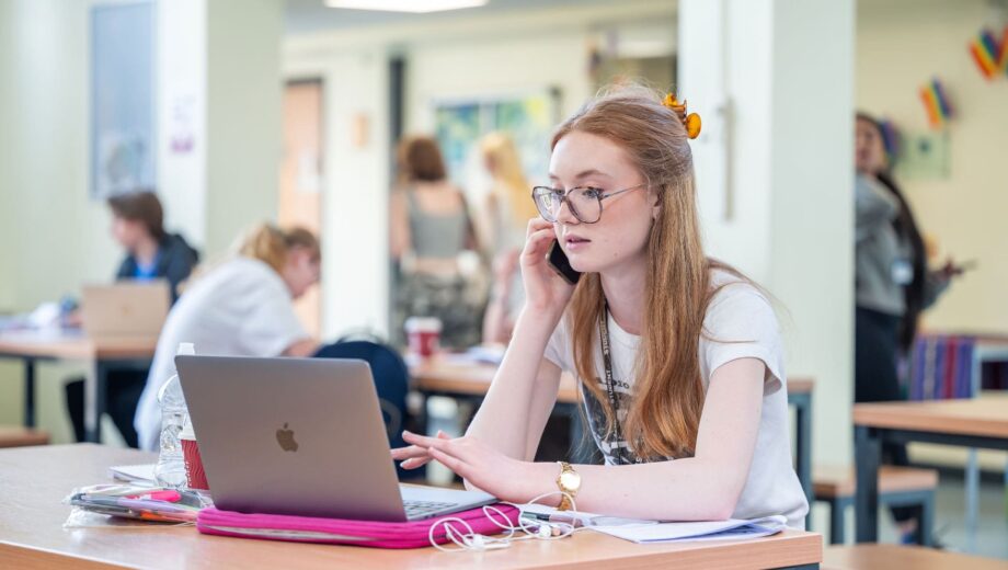 A student on her phone whilst using her laptop.