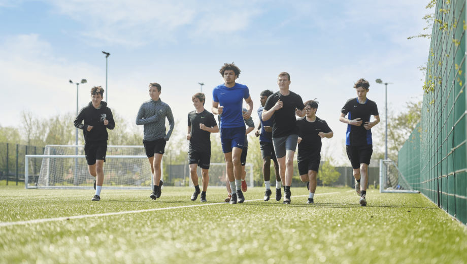 Row of male students running with a football. st helens college