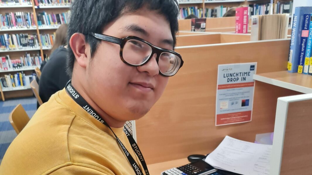 Image of a male student wearing a yellow jumper in the library