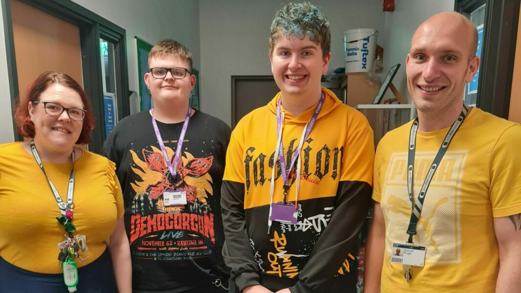 2 students and 2 tutors wearing yellow stood in a corridor