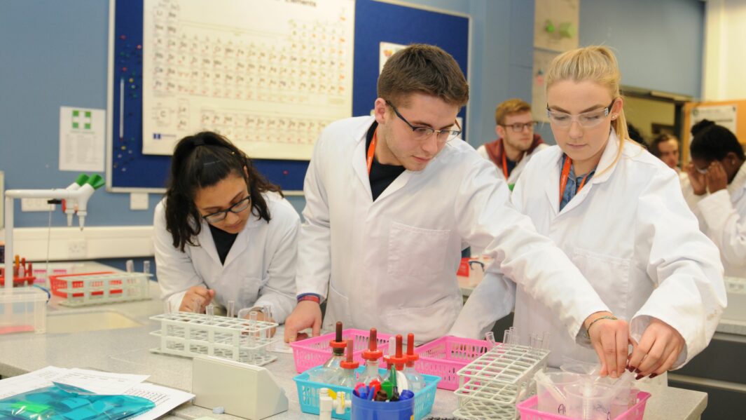 Male and female HE students wearing lab coats doing experiments at Carmel College