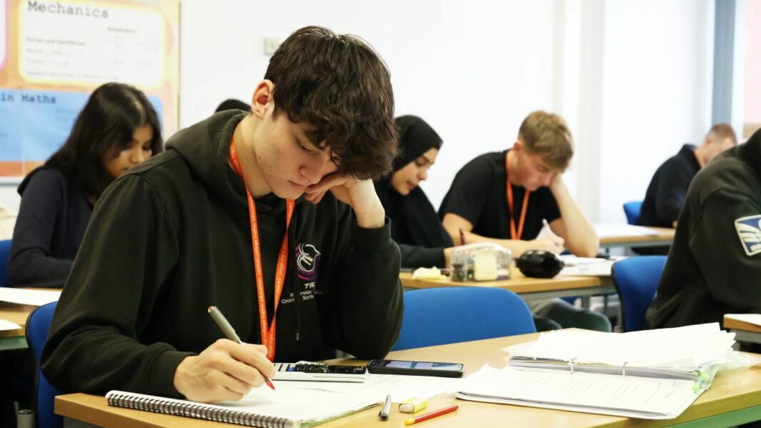 Male HE students working in a Maths classroom writing on a pad