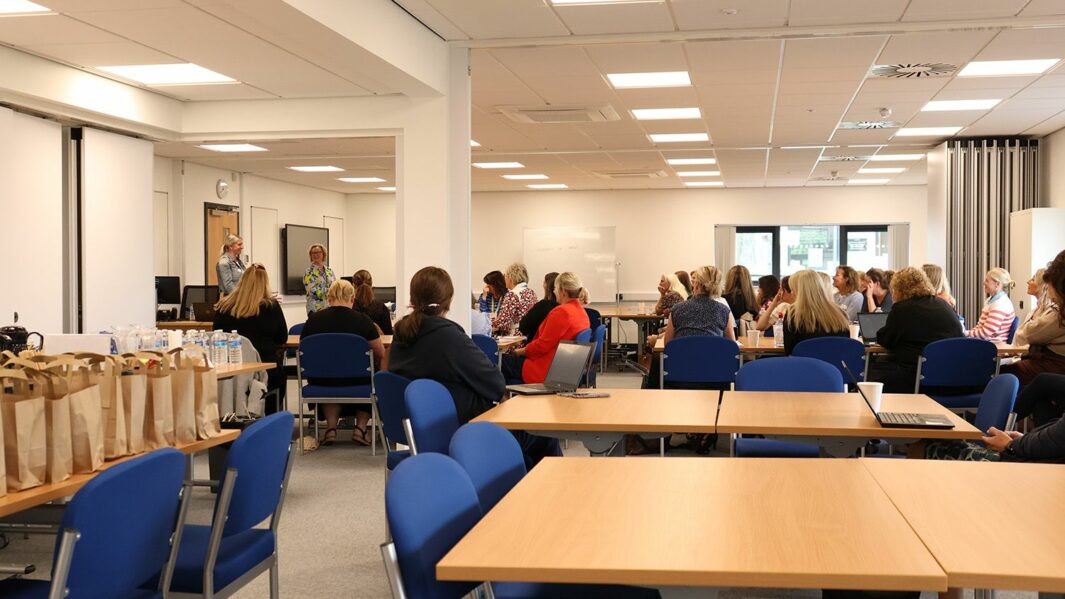 Image of a meeting room with desks and people in a conference