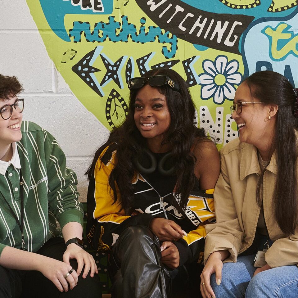 3 students laughing together sat on a bench in the cafe at Carmel