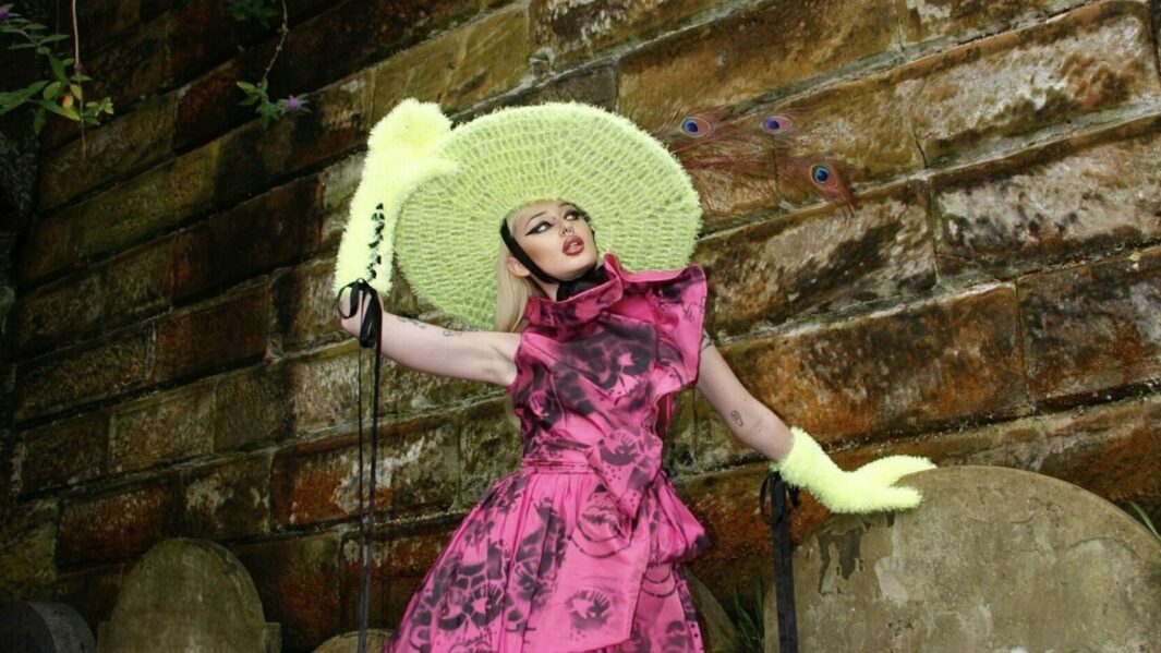 model posing against brick wall in green hat and purple dress