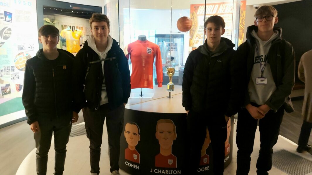 4 students posing in front of England shirt in museum
