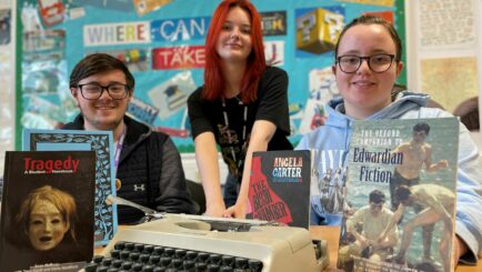 3 English students in a classroom sat at a desk with books