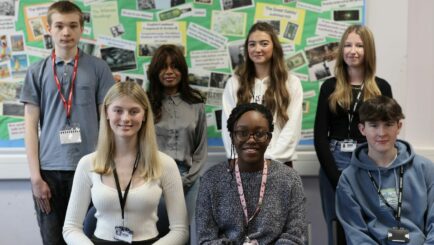 Group of male and female students pictured in a classroom in 2 rows.