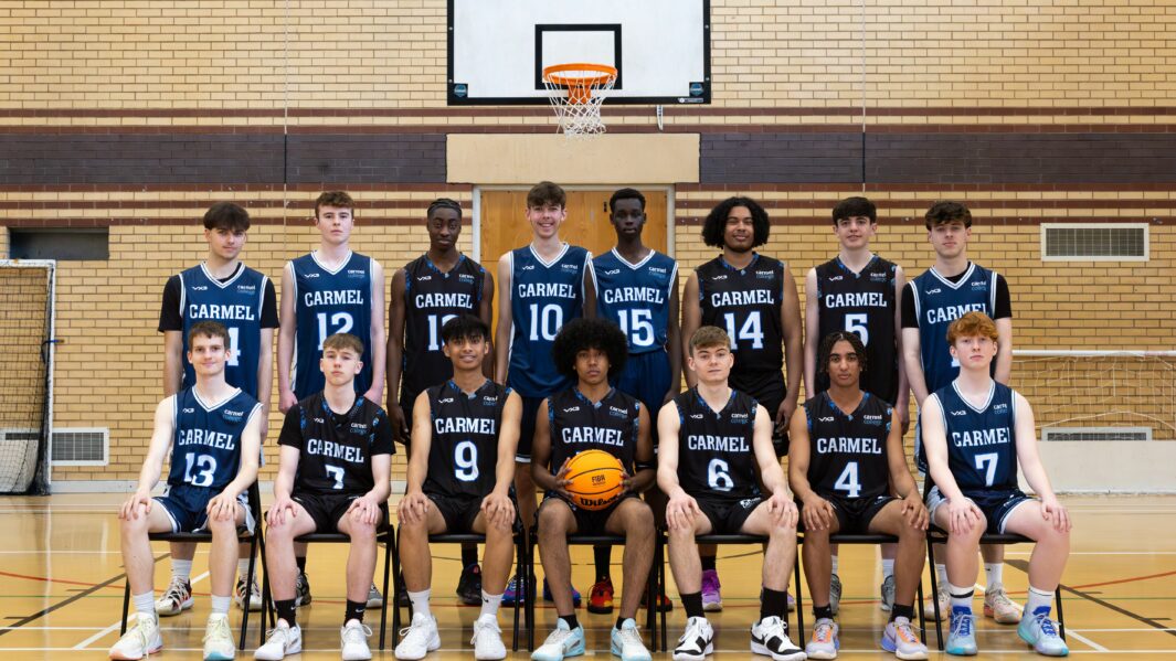 The basketball team of boys stood in a line. Middle boy holding a basketball
