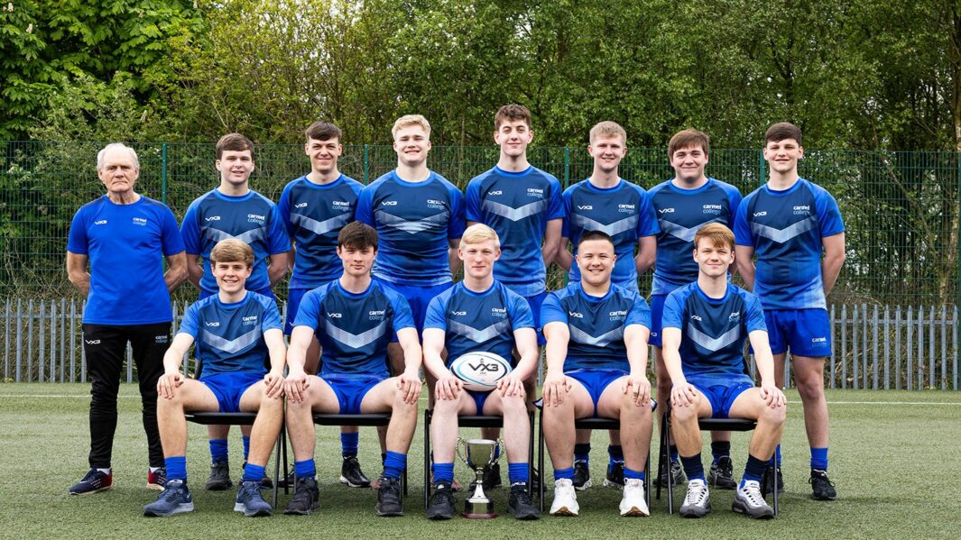 The rugby team of boys stood in a line. Middle boy holding a rugby ball.