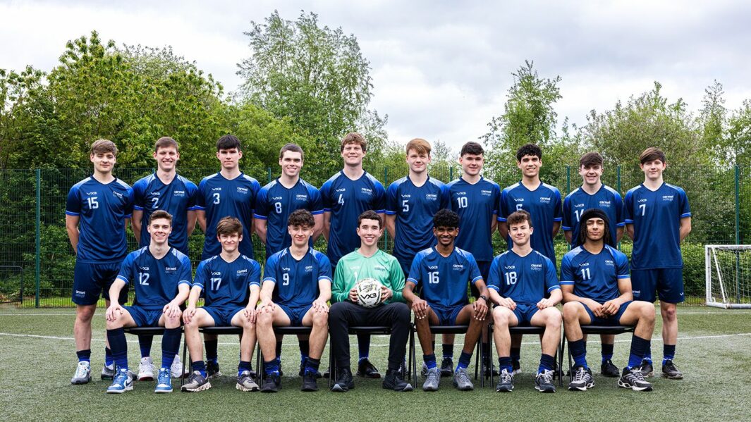 The football team of boys stood in a line. Middle boy holding a football.