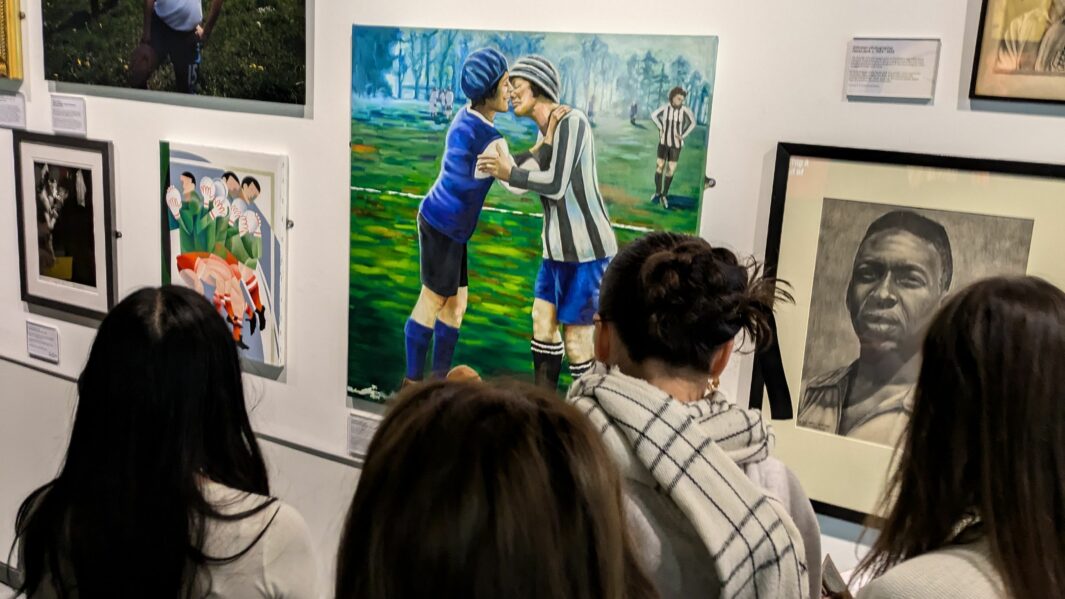 A group of female students looking at artwork on a wall of two footballers kissing