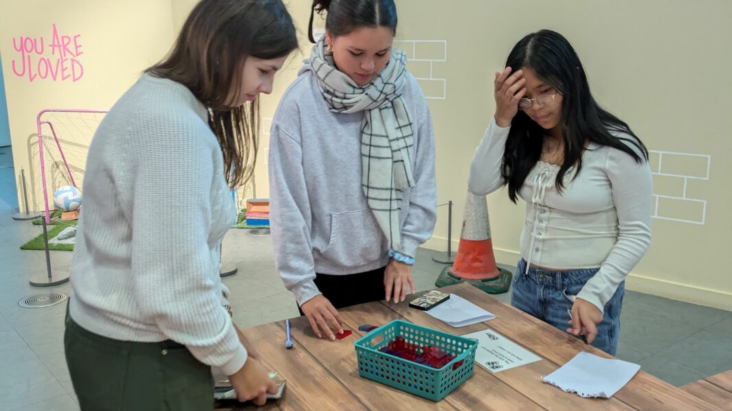 3 female students working at a desk in a gallery space