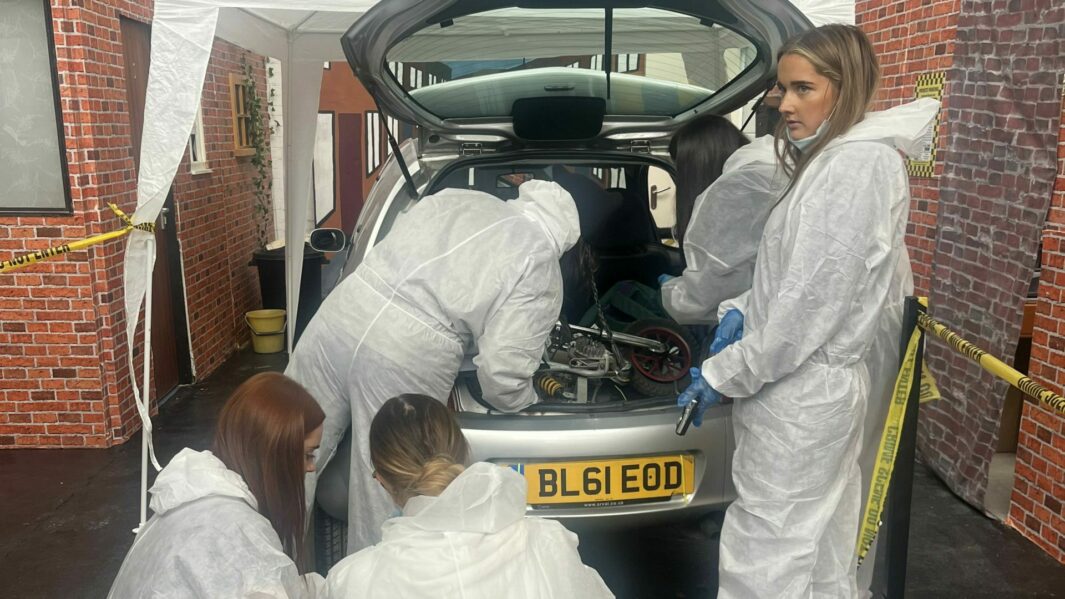 Students in CSI bunny suits collecting evidence from a car