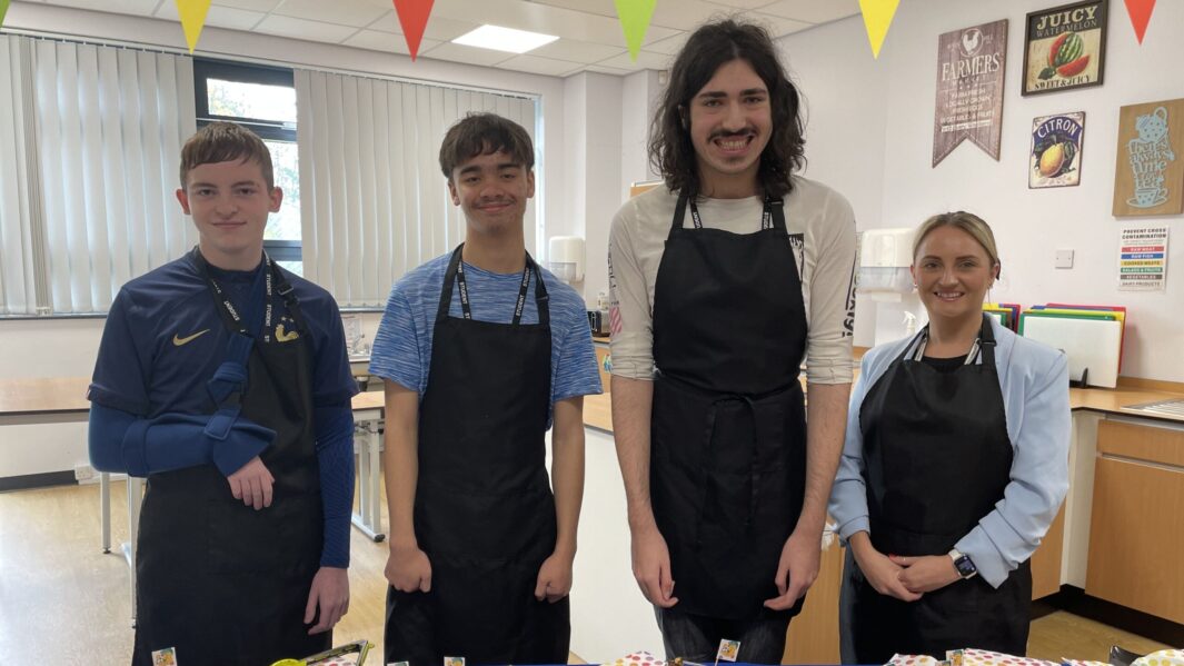 4 foundation students wearing aprons behind their cake stall