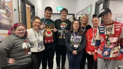 Staff and students in Foundation Learning wearing Christmas jumpers stood in a group in the corridor
