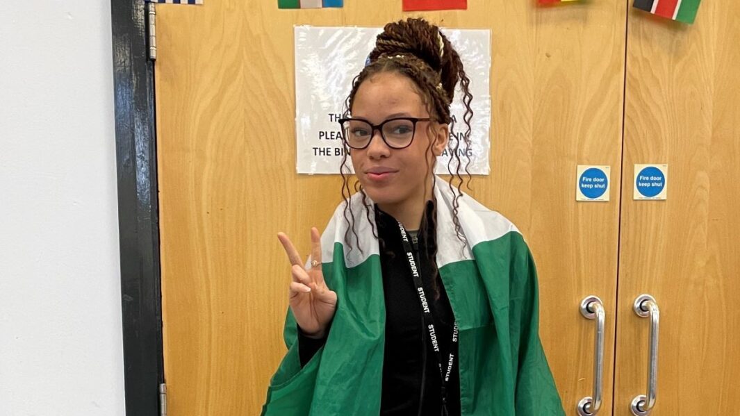 Single female student wearing flag around shoulders in from of flag bunting on Carmel Cultural Appreciaiton Day 2024.