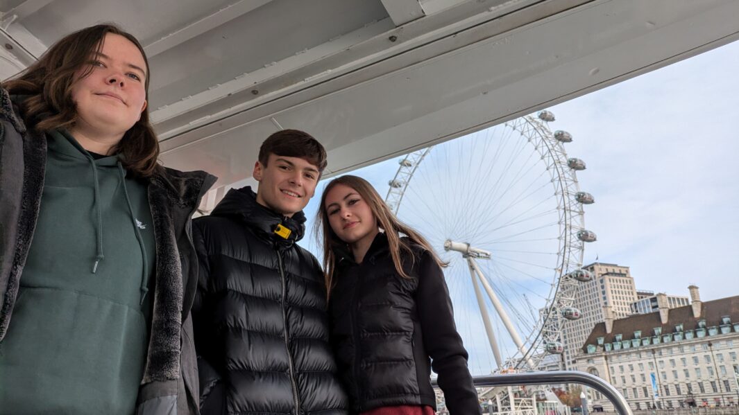 Three Carmel students standing on ferry posing in front of the London Eye.
