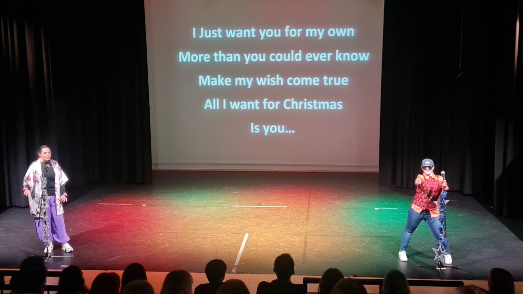 Two BTEC Performing Arts students stand on stage with microphones performing sing a long to All I Want for Christmas.