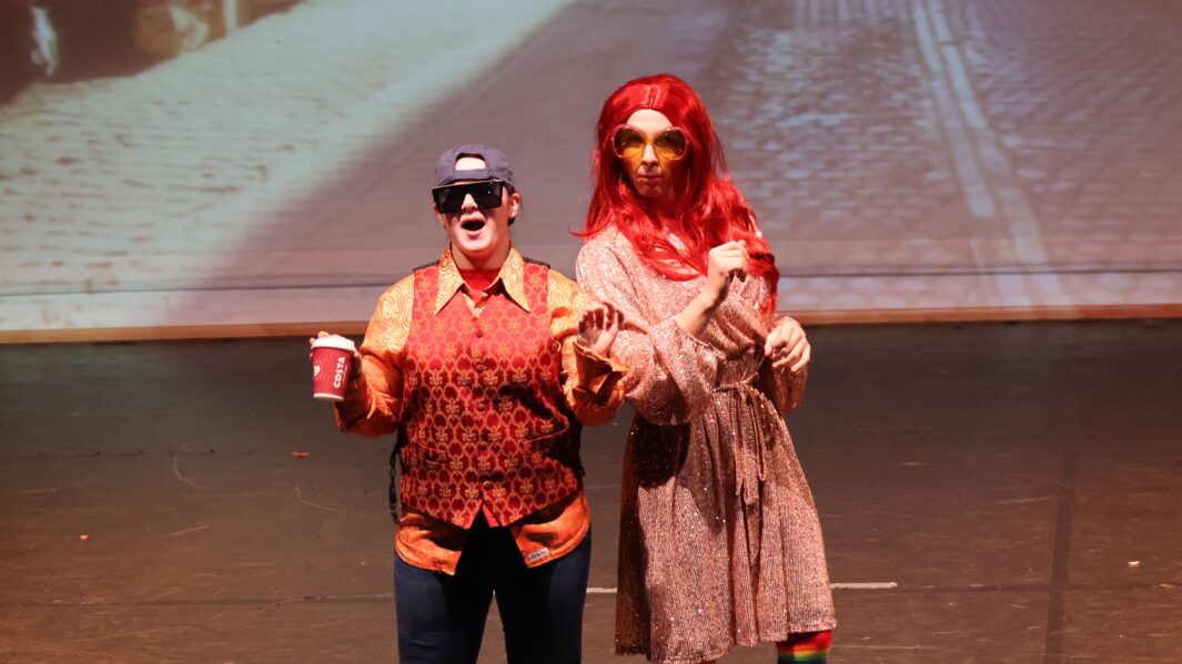 Carmel's Pantomime Dame poses in reg wig and sunglasses with son wearing a cap, sunglasses and holds a coffee cup.