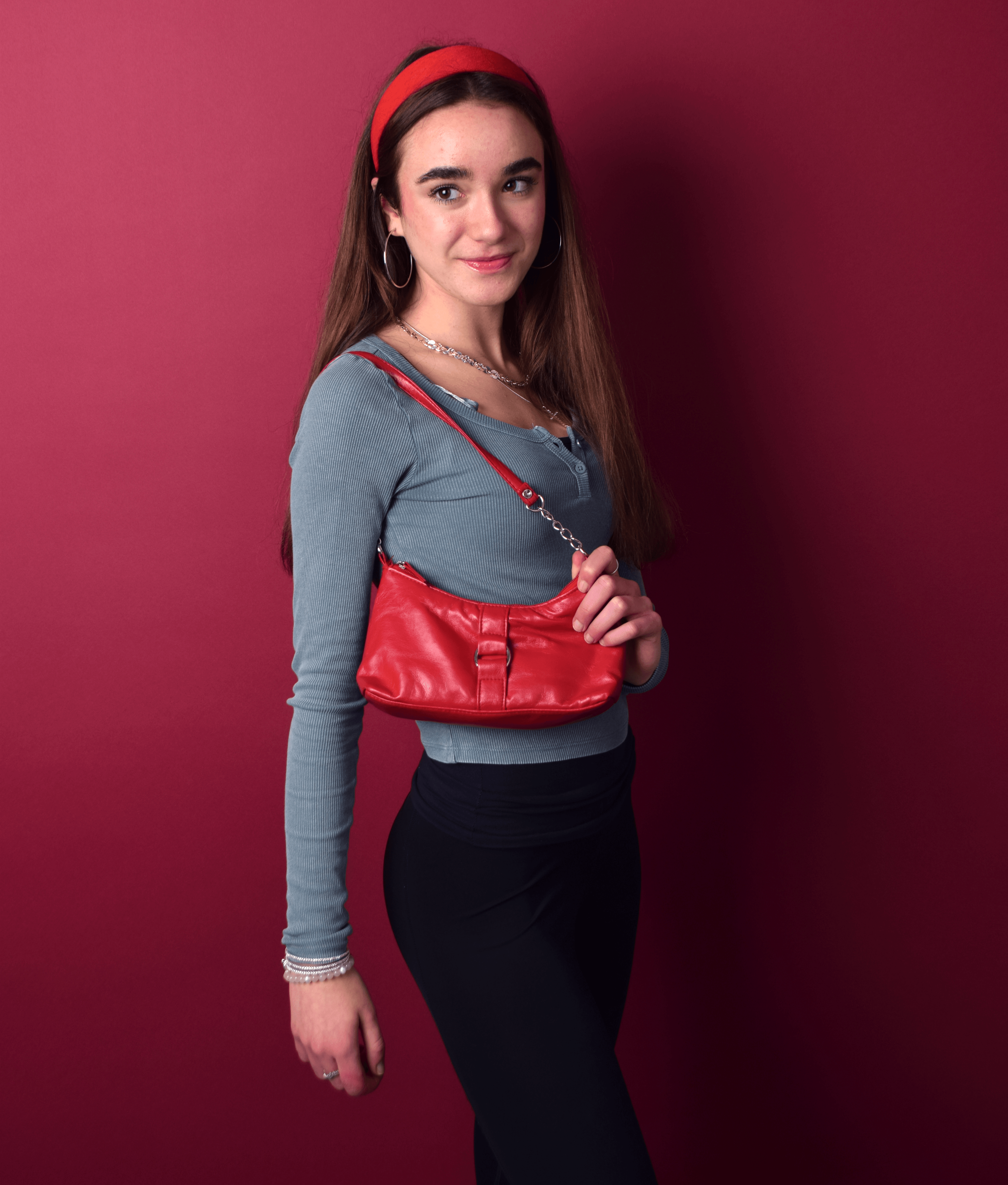 Female student poses with red accessories in front of burgundy background as part of photography shoot.