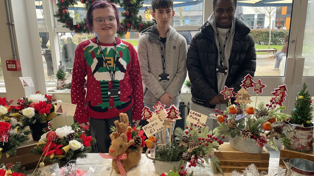 Foundation Learning students wear festive jumpers in front of festive crafts at Christmas Market 2024.