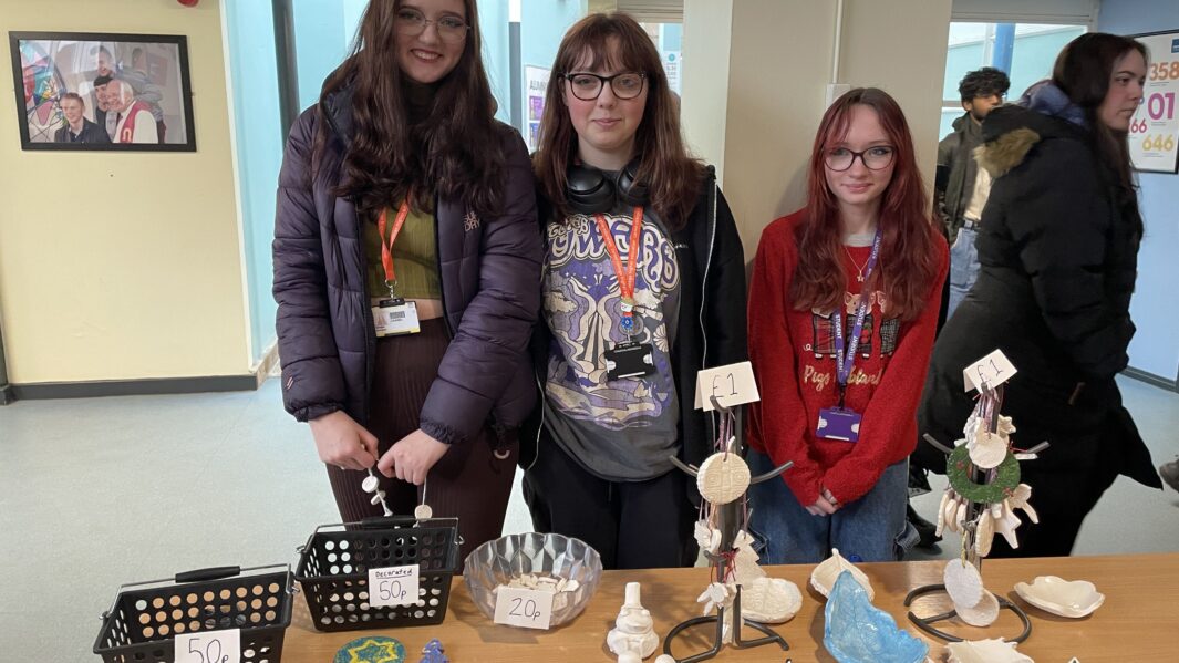 Three female student stallholders showcase handmade clay crafts.