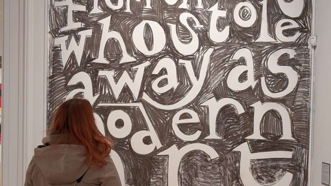 A girl stood looking at large artwork with lettering on
