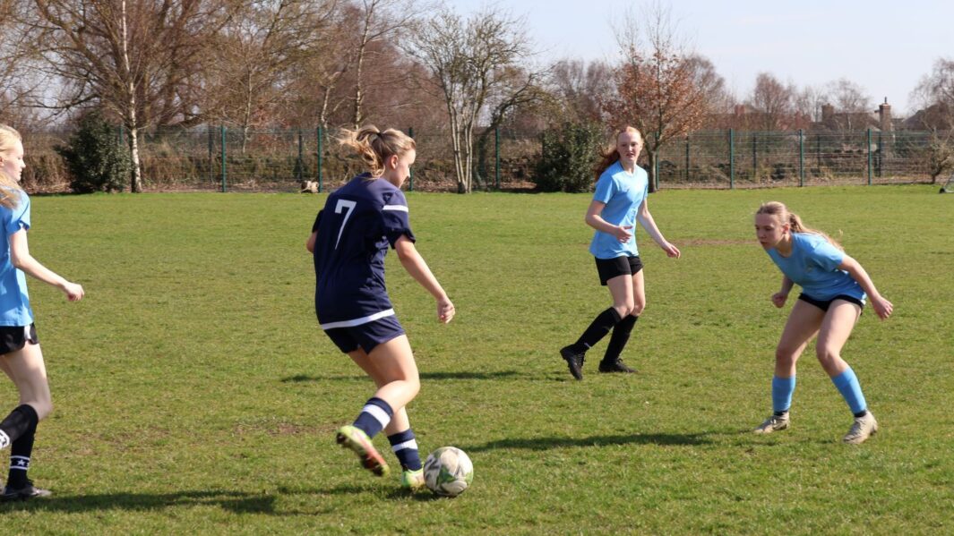 Girls football match one team in dark blue one team in light blue, kicking a ball