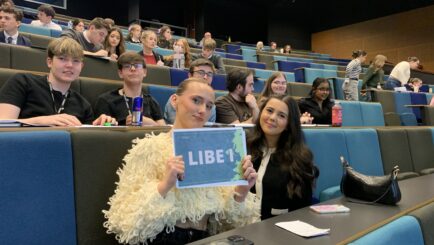 Female student sat holding a sign that says LIBE 1 and male and female students sat around her