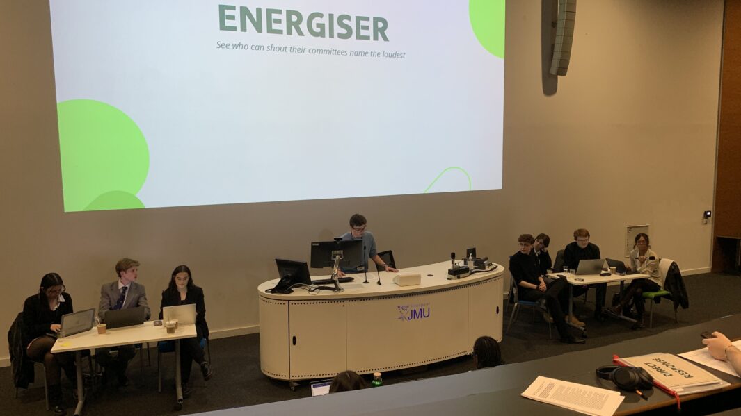 Students sat behind a desk giving a speech