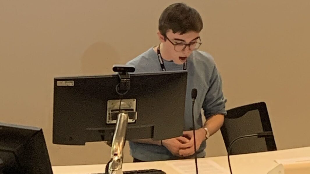 Students sat behind a desk giving a speech