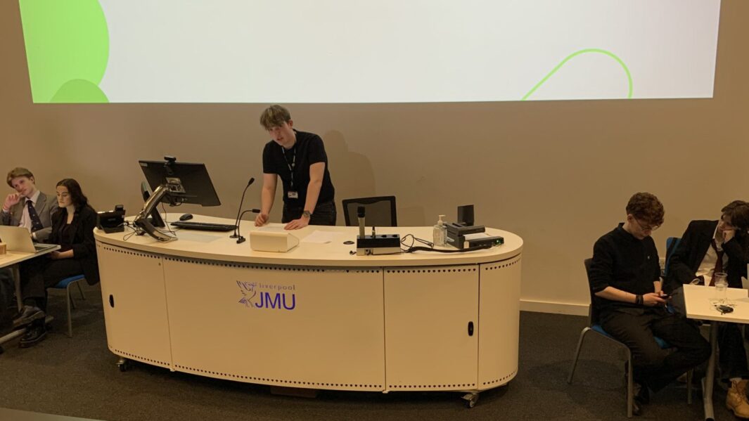 Students sat behind a desk giving a speech