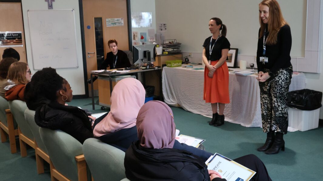 adult stood talking to room of students