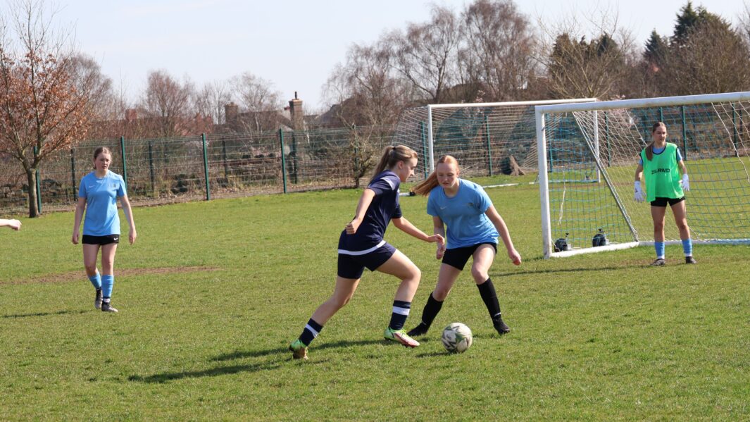 Girls football match one team in dark blue one team in light blue, kicking a ball