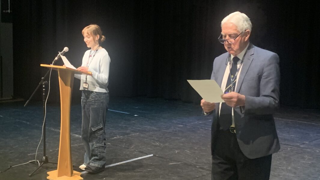 male speaker holding paper, female student stood at alter speaking