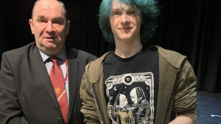 Male in suite stood on the left and student stood to the right holding a trophy