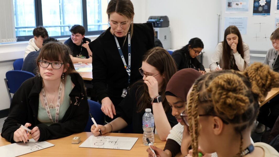 A group of maths students at a desk with the Head of Maths helping