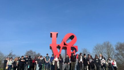 80 students stood in front of a red sign that spells LOVE L O on top VE underneath