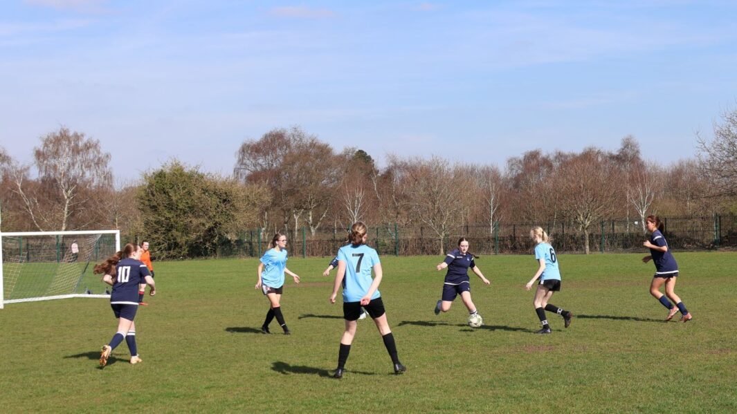 Girls football match one team in dark blue one team in light blue, kicking a ball