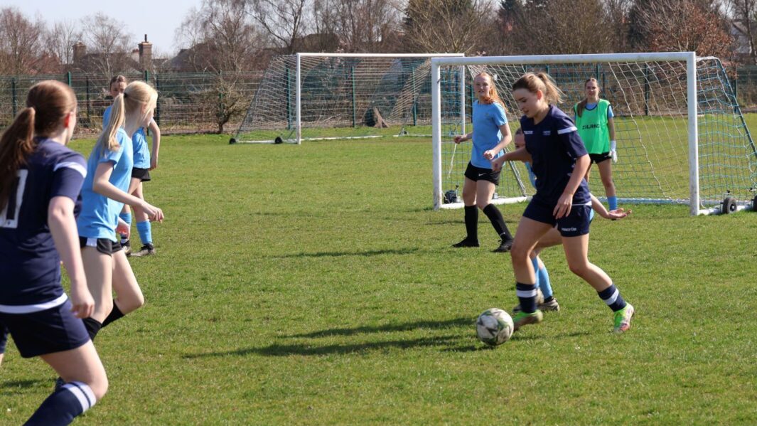 Girls football match one team in dark blue one team in light blue, kicking a ball