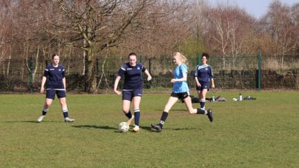 Girls football match one team in dark blue one team in light blue, kicking a ball