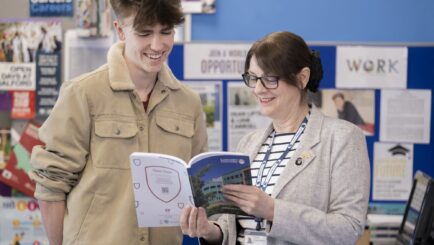 Careers Tutor stood holding a book, showing it a male student