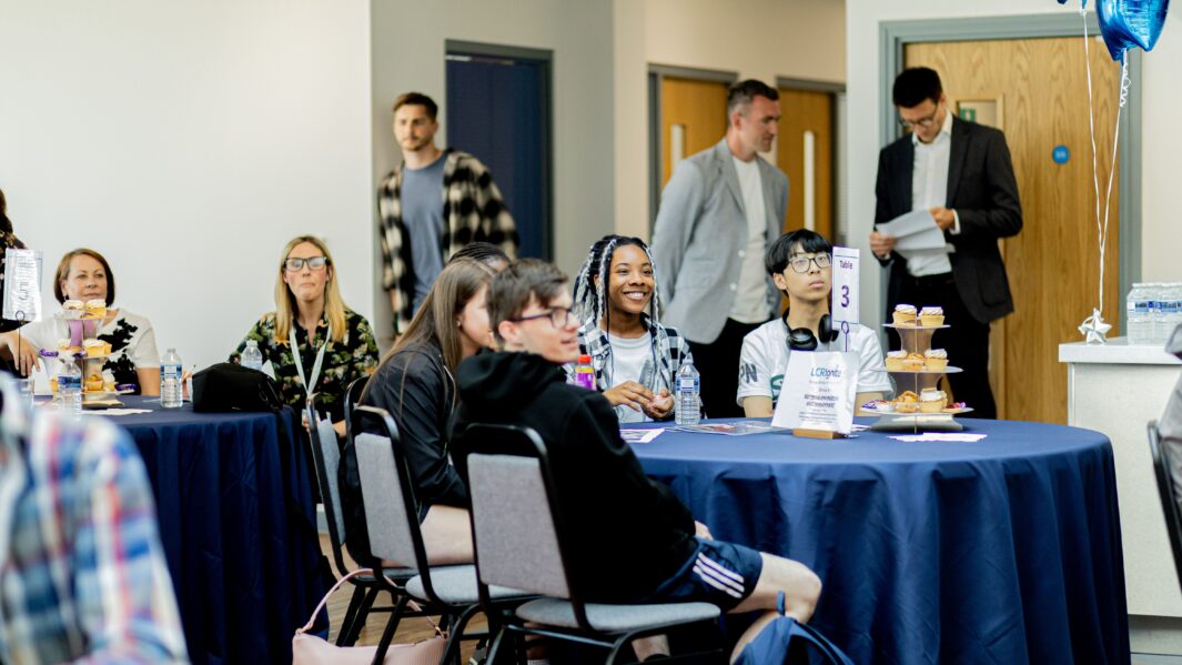 Group of students sat at a table laughing and smiling