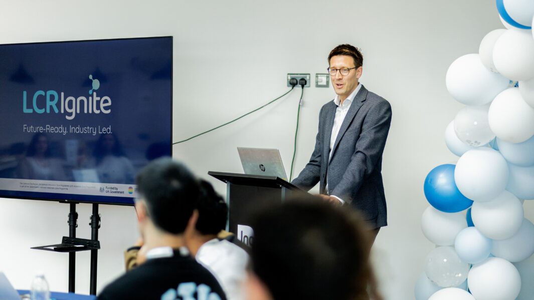 Male CEO stood being laptop talking to room of students
