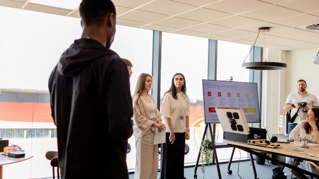 Male and female students stood in boardroom giving a presentation to a panel of judges